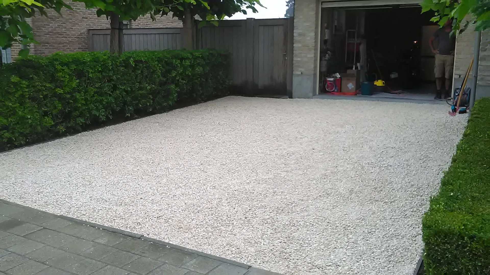 Oprit in licht grind met boordstenen voor een garage, tussen geschoren hagen