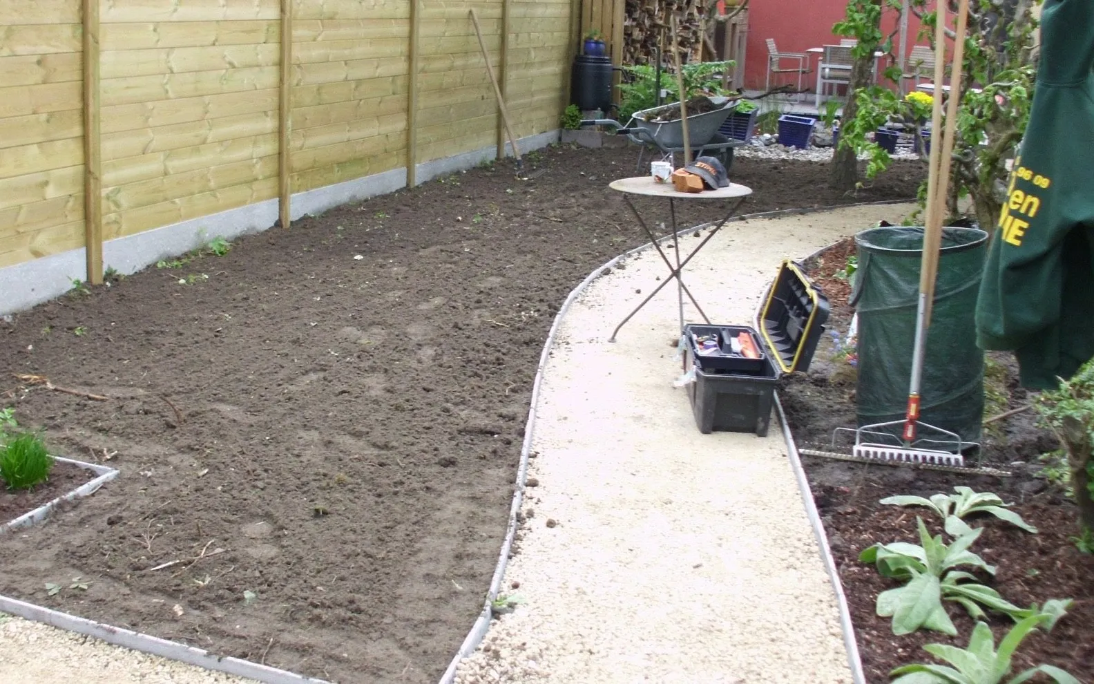 Stadstuin voor de werken: kale grond naast een gebogen grindpad, langs een houten schutting